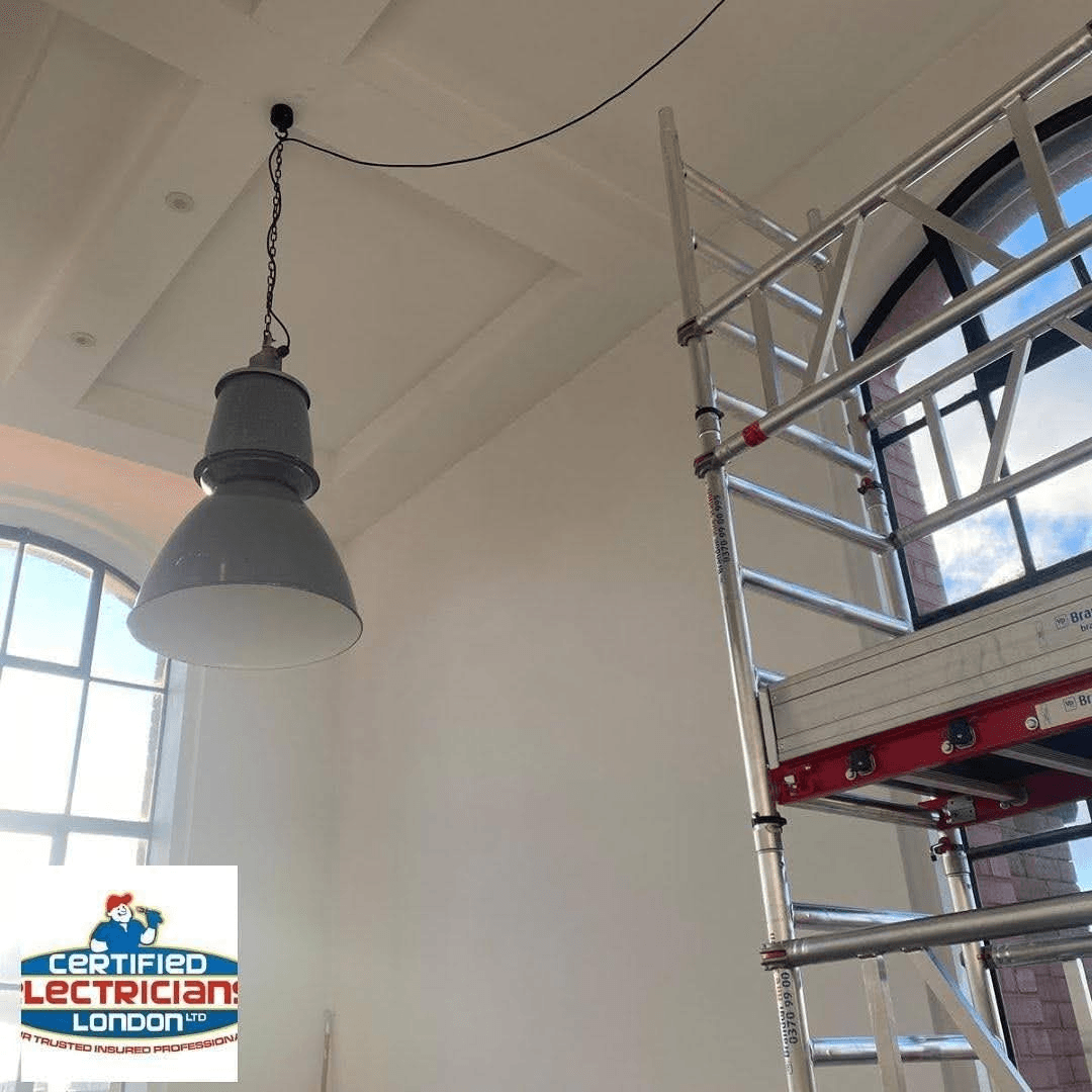 Certified electrician working on industrial lighting with scaffold access